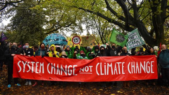 a large group of people holding a red banner with white letters reading system change not climate change
